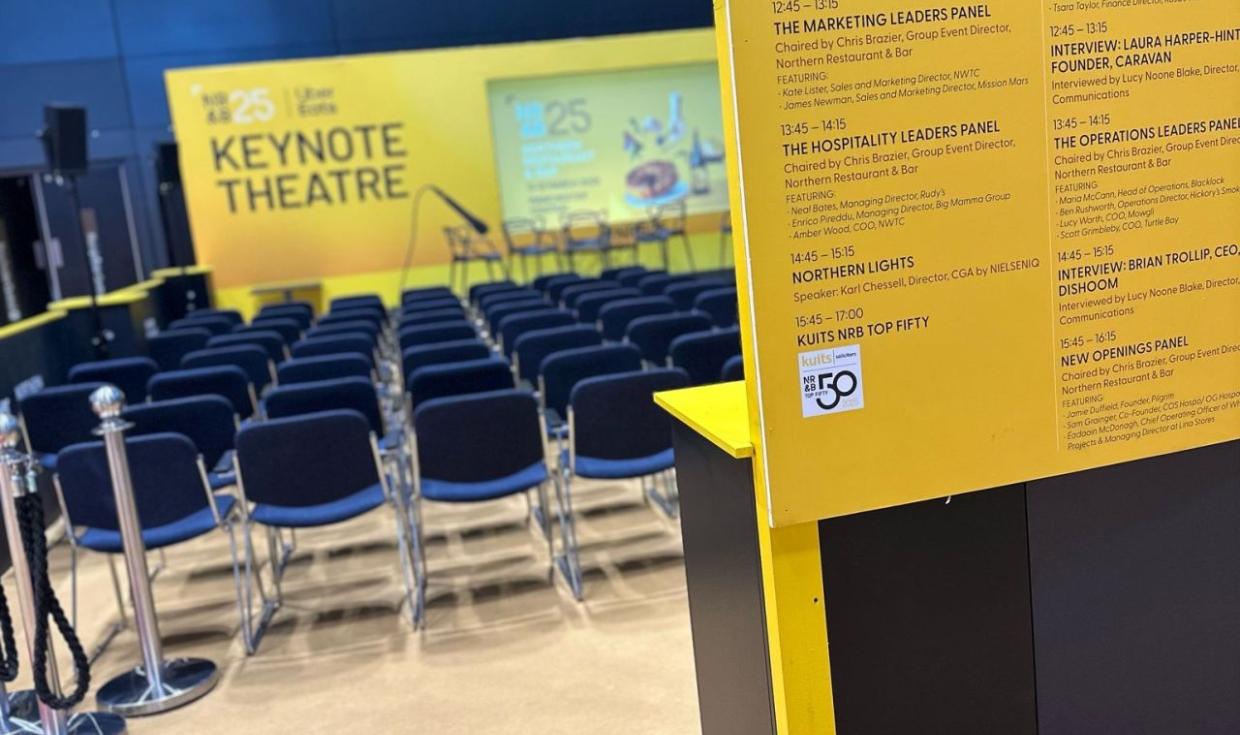 Set up of NRB Keynote Theatre, with Thatre stge and audience seating in background, and line up informational board in foreground. 