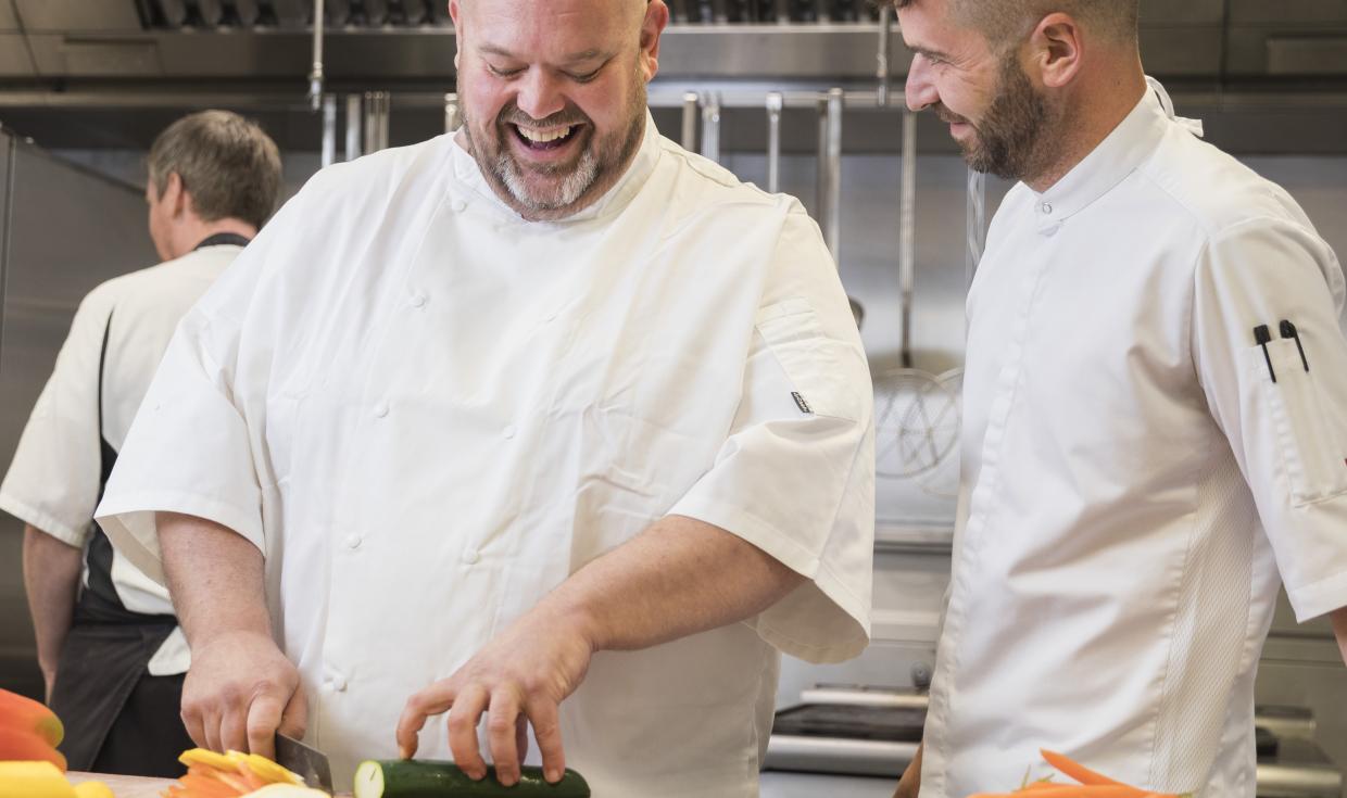 Rik and Matt, dressed in chefs white, smiling whilst stood in Manchester Central's kitchen.