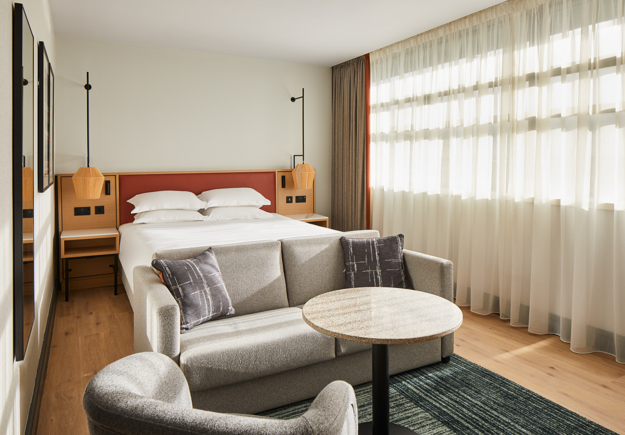 Deluxe King Room with bed, sofa, table and table in an airy room with window stretching whole length of wall