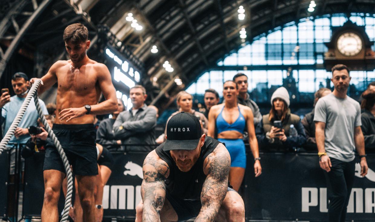 HYROX competitor pulling rope a tone of the stations, with arch and clock of Manchester Central in the background