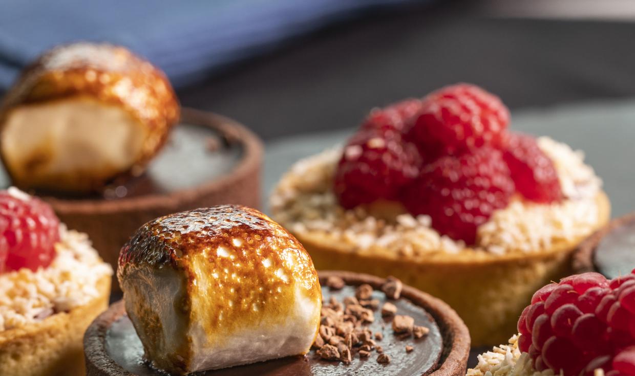 A close up shot of sweet tarts, one is chocolate topped with marshmallow, the other is topped with raspberries