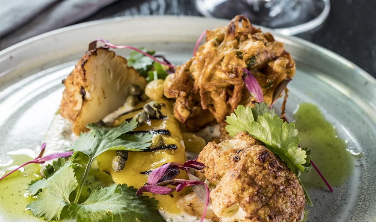 A plate with cauliflower, leaves, and fried vegetables beautifully presented on a dinner table.