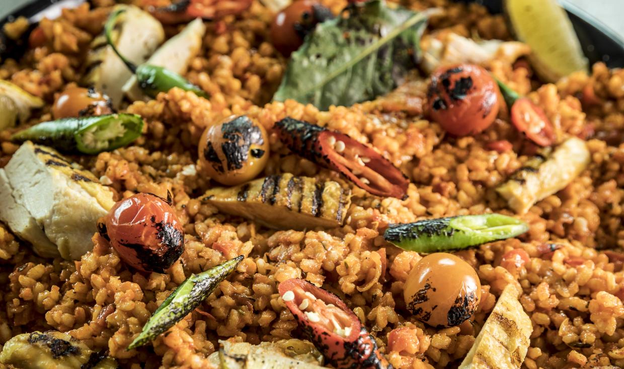 Paella presented in metal paella dish, dressed with lemons and torched tomatoes