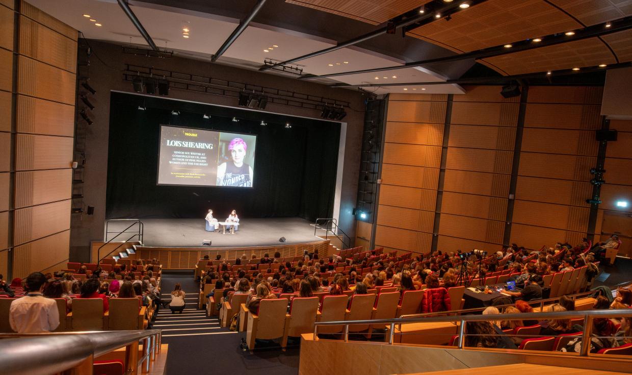 A shot from the back of the Exchange Auditorium as attendees sit watching Caitlin Moran and host on stage talking.