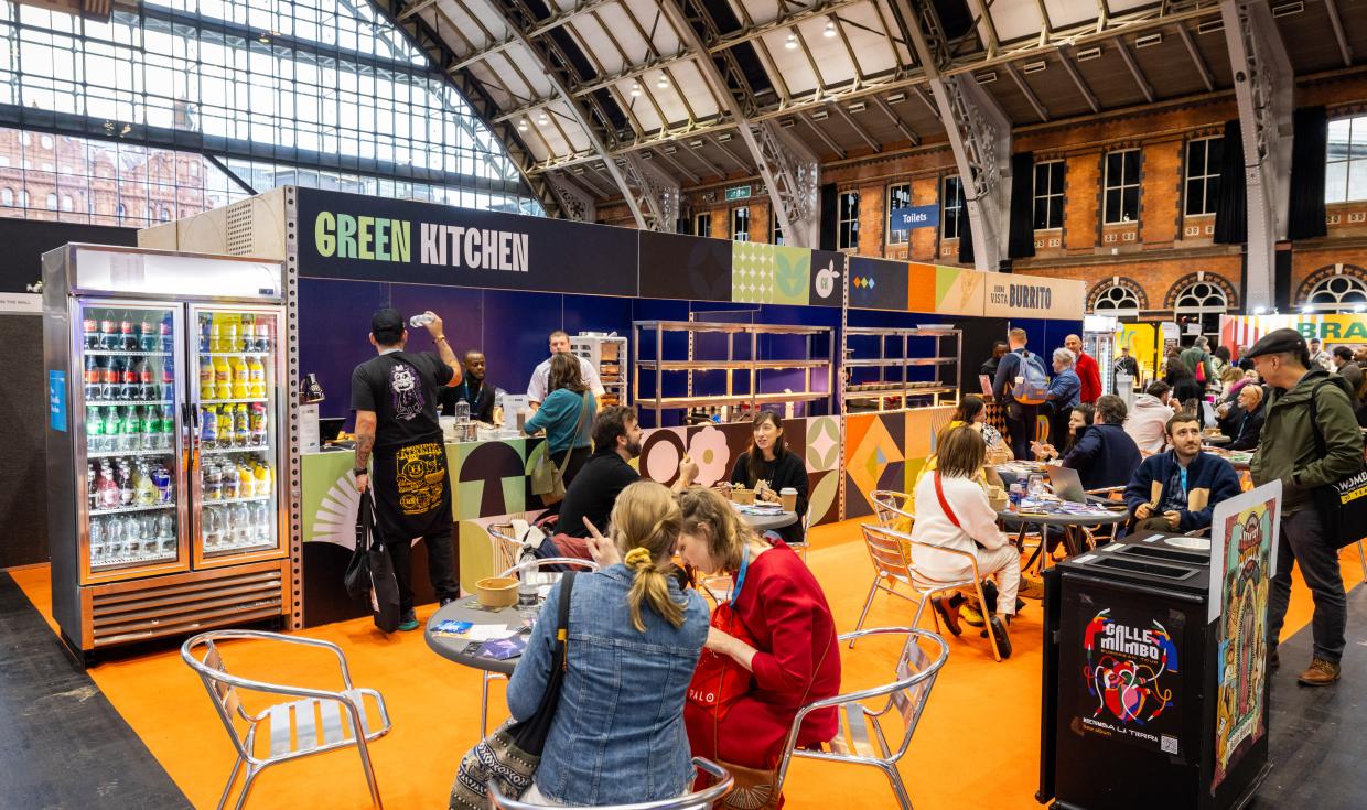 Green Kitchen retail point in Central Hall, with table, chairs and event attendees sat enjoying food in front.